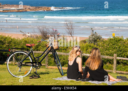 Deux jeunes adolescentes avec cycle vélo'chat assis sur un tapis de pique-nique avec vue sur la plage d'eau douce,Sydney, Australie