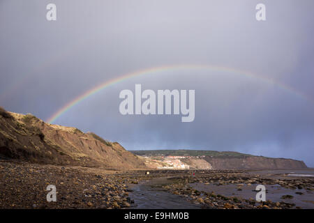 Arc-en-ciel voûtant sur le rivage rocheux et les falaises côtières sur la côte du Yorkshire du Nord après une averse qui passe Banque D'Images