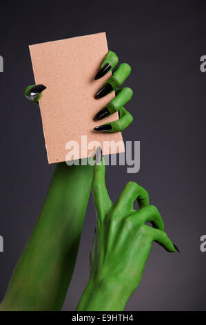 Monstre vert mains avec ongles tenant noir morceau de carton, thème de l'Halloween Banque D'Images