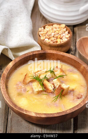 La soupe aux pois avec lard et croûtons au bol en bois sur table rustique Banque D'Images