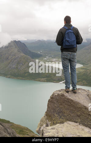 Jeune homme debout sur le bord de Besseggen crête de montagne surplombant le lac Gjende et les montagnes environnantes. La Norvège. Banque D'Images