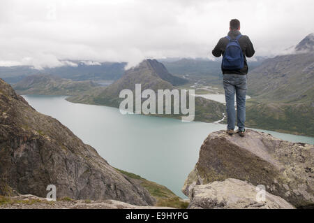 Jeune homme debout sur le bord de Besseggen crête de montagne surplombant le lac Gjende et les montagnes environnantes. La Norvège. Banque D'Images