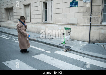 Un vieil homme promène son chien dans les rues de Paris lors de l'utilisation d'un téléphone. Banque D'Images