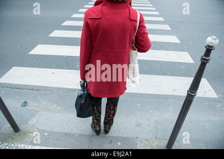 Une femme à paris marche à travers un carrefour portant une veste rouge Banque D'Images