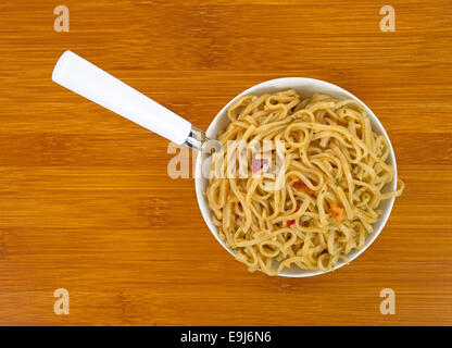 Fermer la vue d'une portion de nouilles chow mein aux crevettes et les assaisonnements dans un petit bol avec une fourchette dans le repas sur une table en bois Banque D'Images