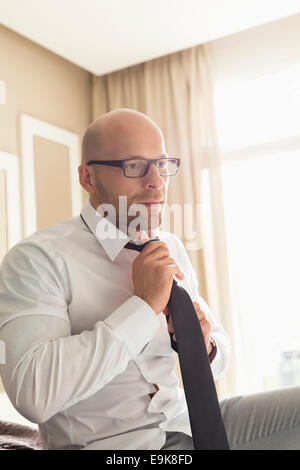 Mid adult businessman adjusting necktie à la maison Banque D'Images