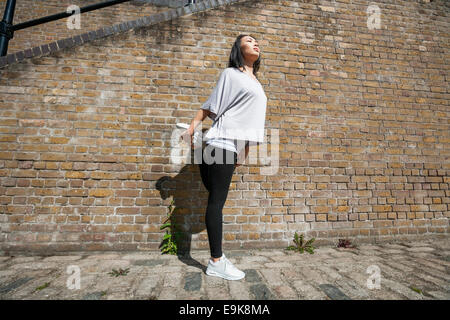 Longueur totale de jeunes fit woman stretching against brick wall Banque D'Images