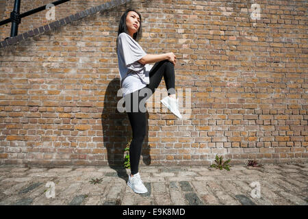 Vue latérale sur toute la longueur des jeunes fit woman stretching against brick wall