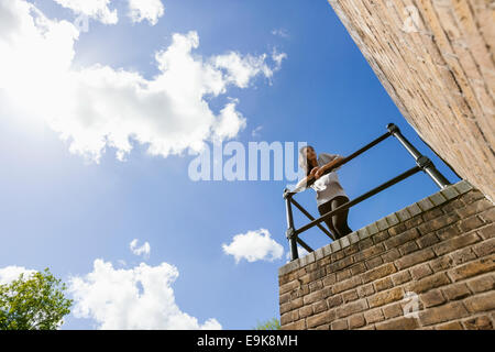 Low angle view of young woman leaning on railing against cloudy sky Banque D'Images