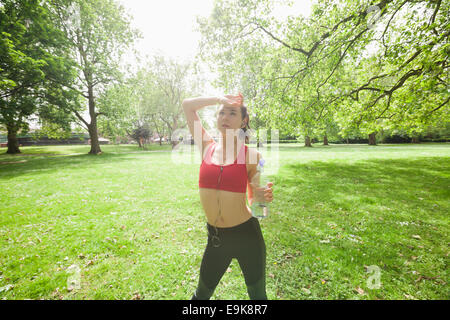 Fatigué fit woman avec bouteille d'eau en écoutant de la musique en park Banque D'Images