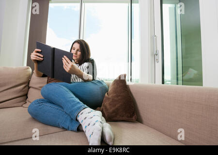 Toute la longueur de young woman reading book on sofa Banque D'Images