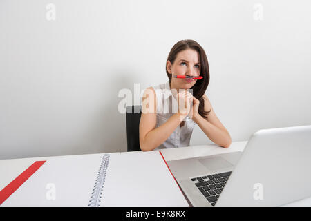Thoughtful businesswoman holding pen sous le nez at desk in office Banque D'Images