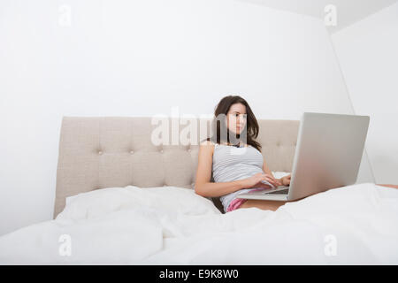 Jeune femme en vêtements de using laptop in bed Banque D'Images