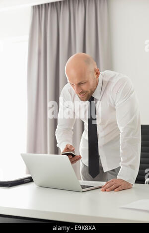 Mid adult businessman using call phone at home office Banque D'Images