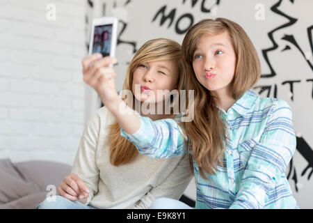 Cute sisters tacaud tout en prenant des photos avec smart phone at home Banque D'Images