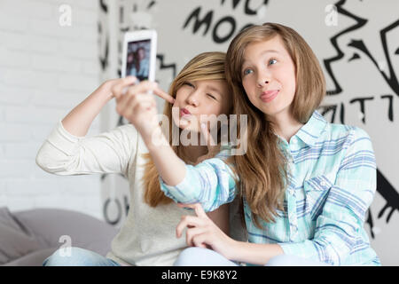 Cute sisters tacaud tout en prenant des photos avec smart phone at home Banque D'Images