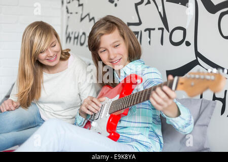 Jeune fille à l'écoute de sœur à jouer de la guitare à la maison Banque D'Images