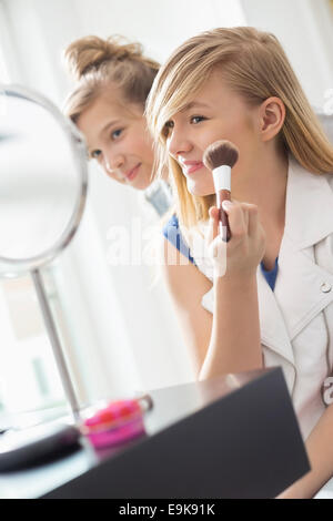 Girl soeur appliquant le maquillage en face du miroir à la maison Banque D'Images