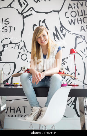 Portrait en pied de teenage girl with skateboard assis sur une table d'étude à la maison Banque D'Images