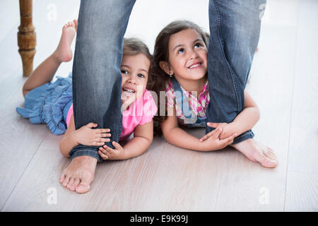 Girls holding ludique père jambes sur plancher de bois franc Banque D'Images