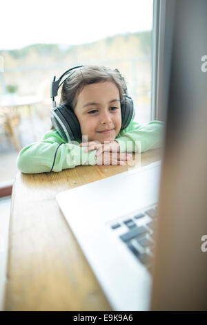 Cute little girl listening to music on headphones while using laptop at home Banque D'Images