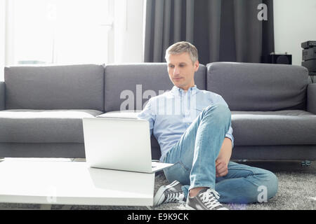 Full-length of man using laptop in living room Banque D'Images