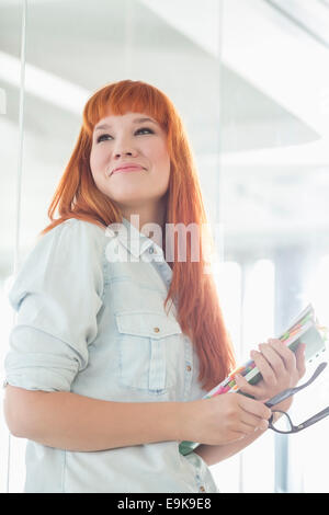 Smiling businesswoman looking away en maintenant des fichiers dans creative office Banque D'Images