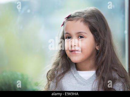 Portrait of cute little girl contre la fenêtre en verre à la maison Banque D'Images