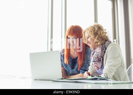 Smiling businesswomen using laptop together in creative office Banque D'Images