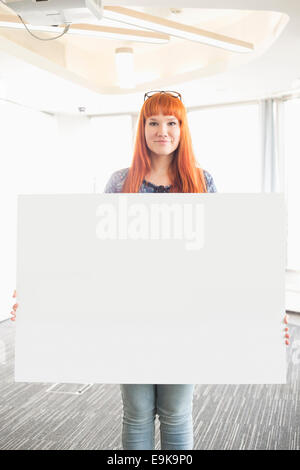 Portrait of businesswoman holding blank placard in creative office Banque D'Images