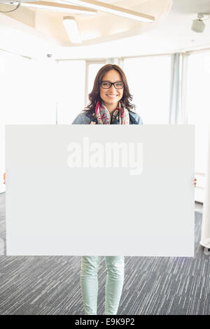 Portrait of happy businesswoman holding blank sign in creative office Banque D'Images