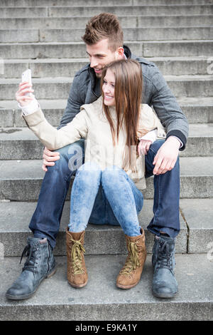 Toute la longueur du couple photo d'eux-mêmes tout en étant assis sur les marches à l'extérieur Banque D'Images