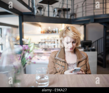 Inquiets young woman reading text message on cell phone in cafe Banque D'Images