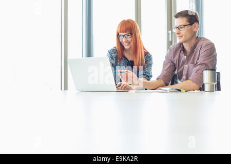 Des collègues d'affaires using laptop at desk in creative office Banque D'Images