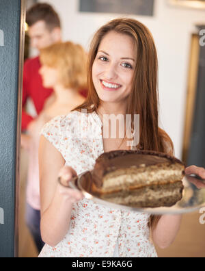 Portrait of happy woman holding cake dans le bac avec des amis en arrière-plan au café Banque D'Images