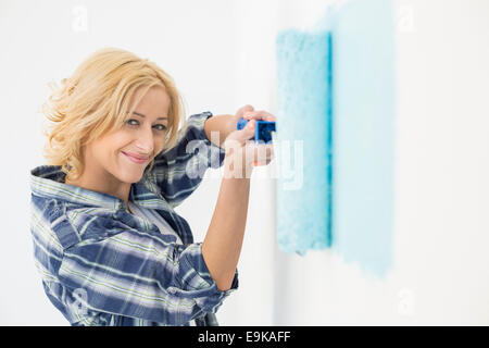 Portrait of Beautiful woman painting wall with paint roller Banque D'Images