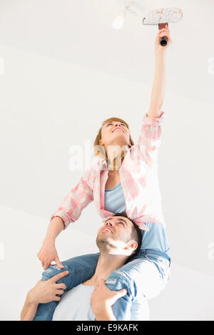 Femme sur les épaules de l'homme peinture plafond avec rouleau à peindre Banque D'Images