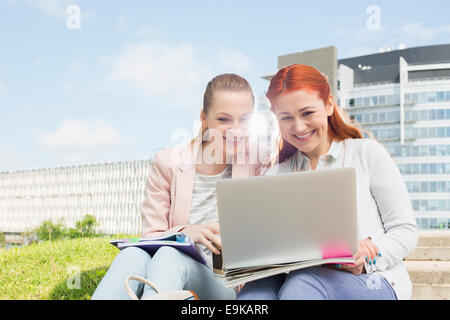 Smiling young university students using laptop avec bâtiments en arrière-plan Banque D'Images