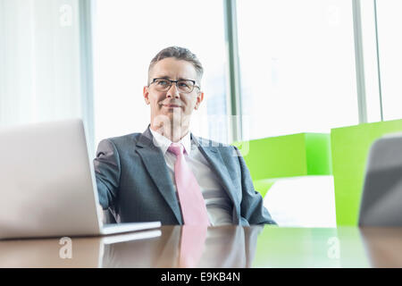 Middle-aged man with laptop sitting at conference table Banque D'Images