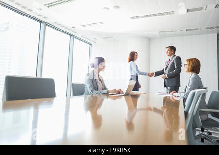 Businessman and businesswoman shaking hands in conference room Banque D'Images