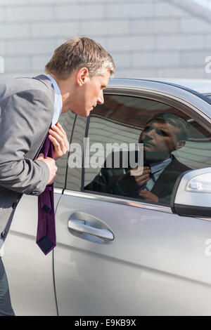 Businessman adjusting tie tout en regardant dans la fenêtre de voiture Banque D'Images