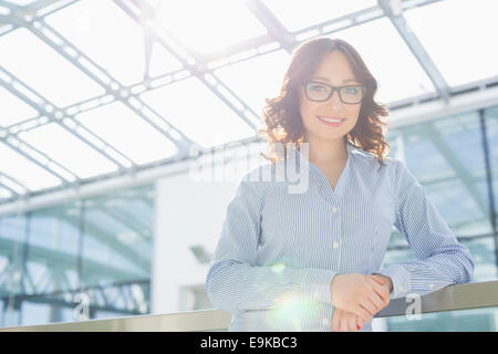 Portrait of happy young businesswoman leaning on railing in office Banque D'Images