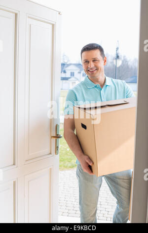 Happy man carrying cardboard box pendant l'entrée nouvelle maison Banque D'Images