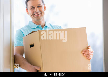 Happy man carrying cardboard box à l'entrée de la nouvelle maison Banque D'Images