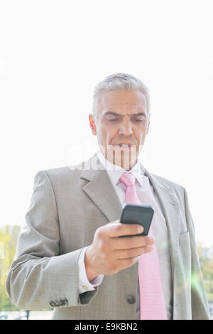 Businessman reading text message on cell phone against sky Banque D'Images