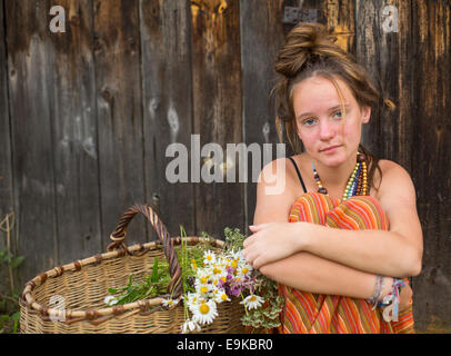 Belle jeune fille dans un cadre rural avec un panier de fleurs sauvages. Banque D'Images