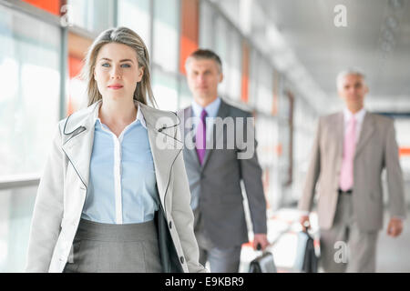 Belle jeune businesswoman walking avec des collègues masculins en arrière-plan à plate-forme du train Banque D'Images