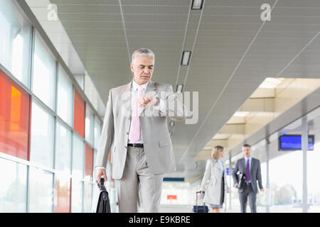 Middle aged businessman contrôle de temps avec des collègues en arrière-plan à la gare de chemin de fer Banque D'Images