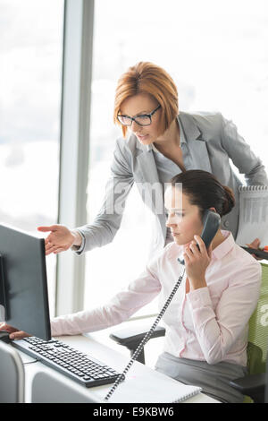 Businesswoman using téléphone fixe le gestionnaire tout en pointant vers computer in office Banque D'Images