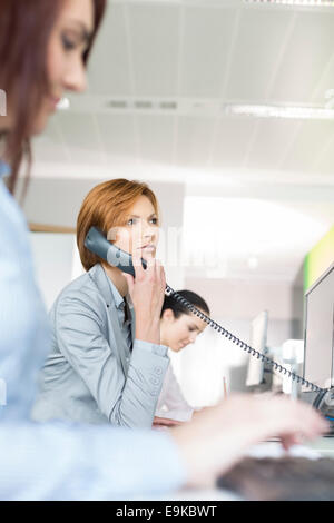 Young businesswoman using landline phone in office Banque D'Images